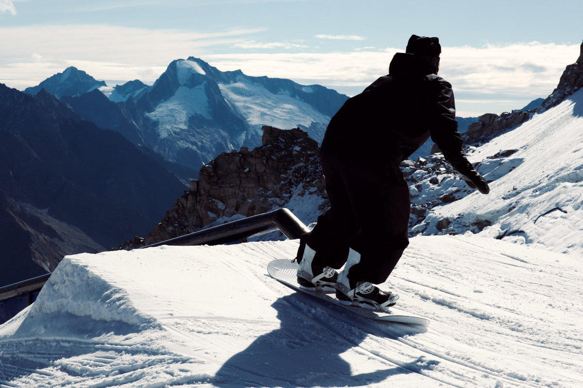 Snowboarder in silhouette riding toward a jump, mountains behind