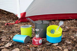 Colorful camping cookware set on the ground in front of a tent.