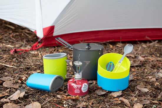 Colorful camping cookware set on the ground in front of a tent.