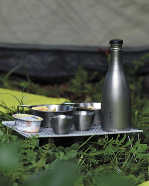 Snow Peak Ozen Solo Table SLV-171 set up outside a tent, holding titanium sake bottle, cups and bowls (not included)