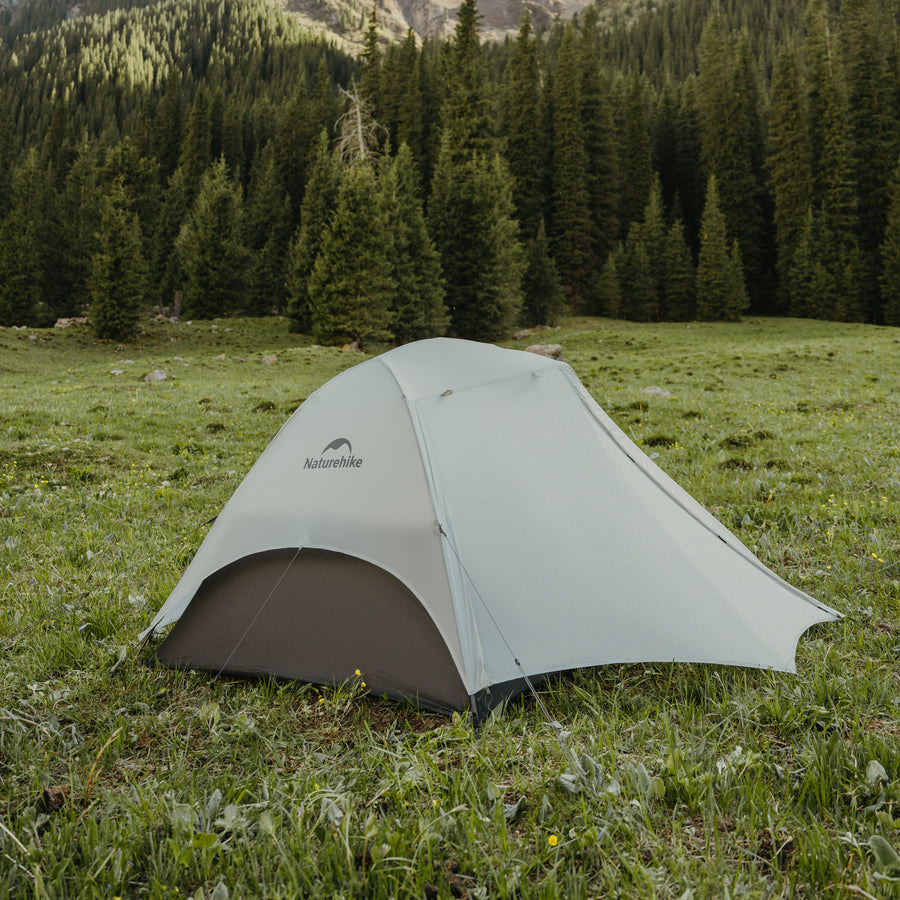 Green tent pitched in a grassy field with trees in the background