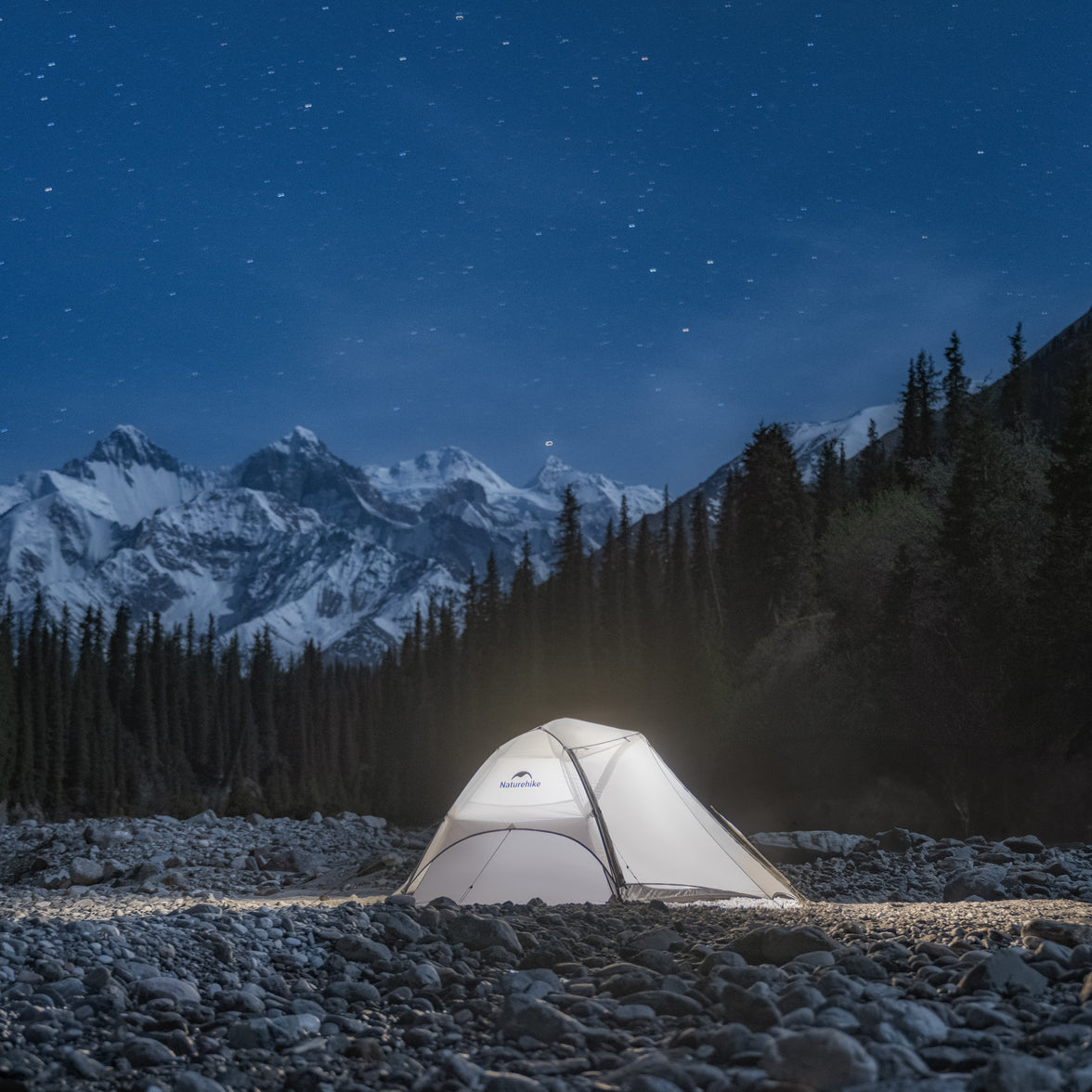 Tent illuminated in a snowy mountain landscape under a starry night sky.