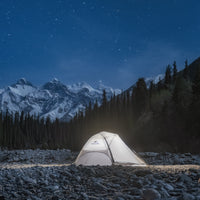 Tent illuminated in a snowy mountain landscape under a starry night sky.