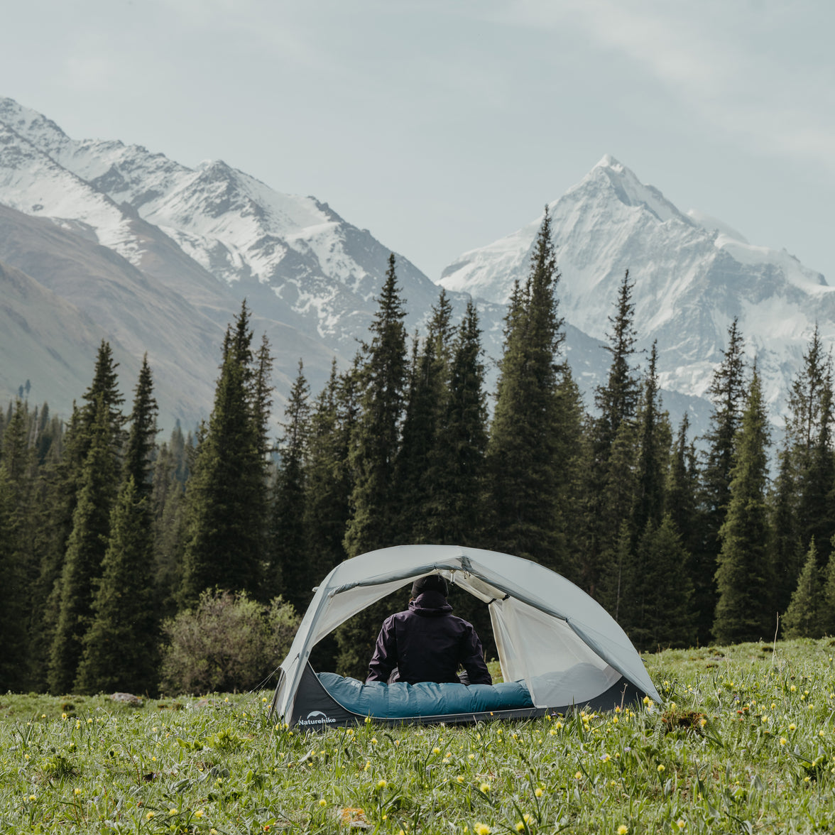 Person inside a tent in a mountainous forest landscape