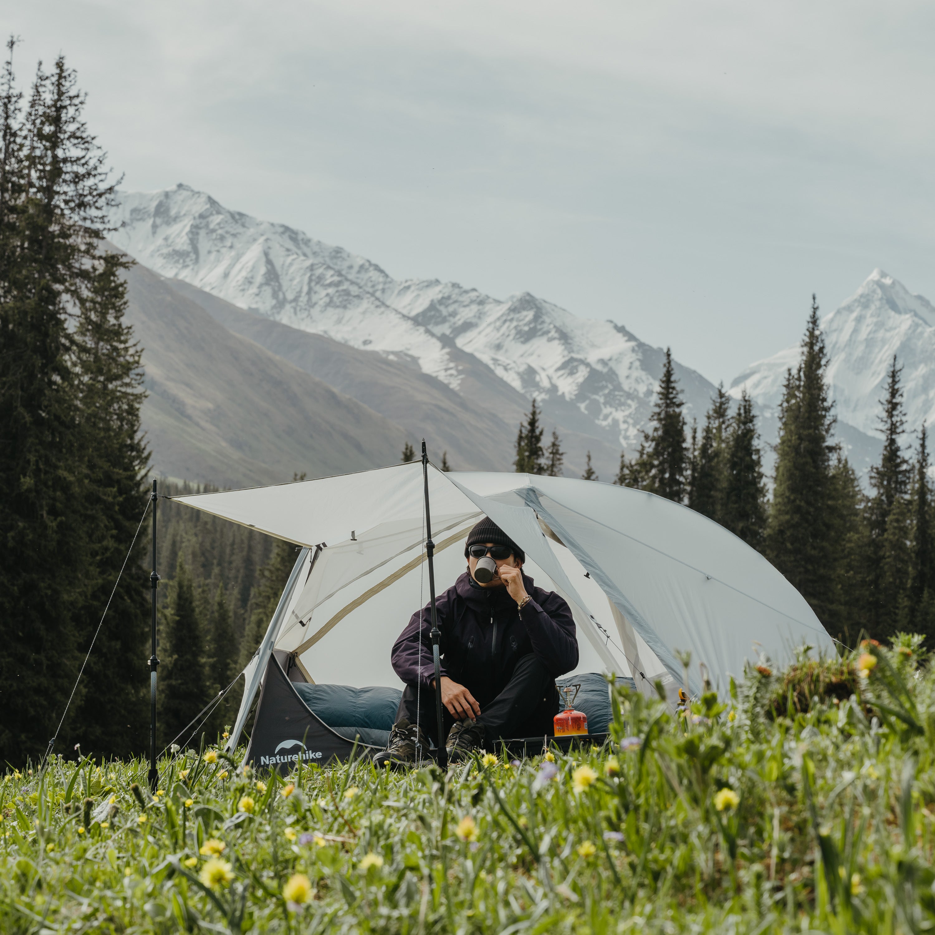Person sitting in front of a tent with mountains and trees in the background