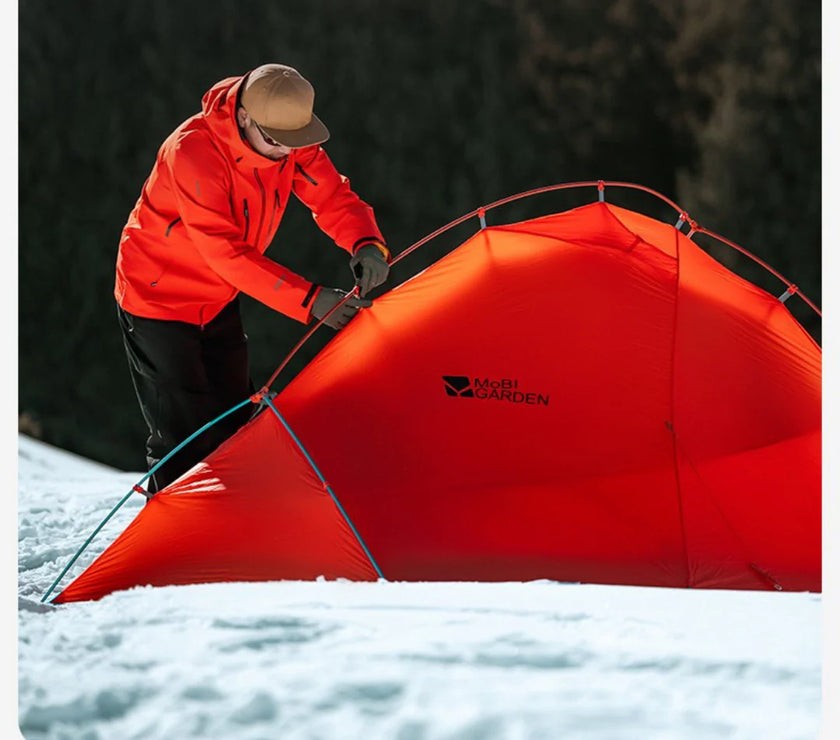 Person setting up a red Marmot tent in a snowy landscape