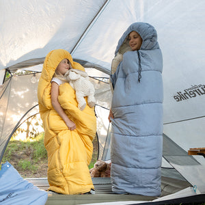 Two children in yellow and blue sleeping bags standing inside a tent.