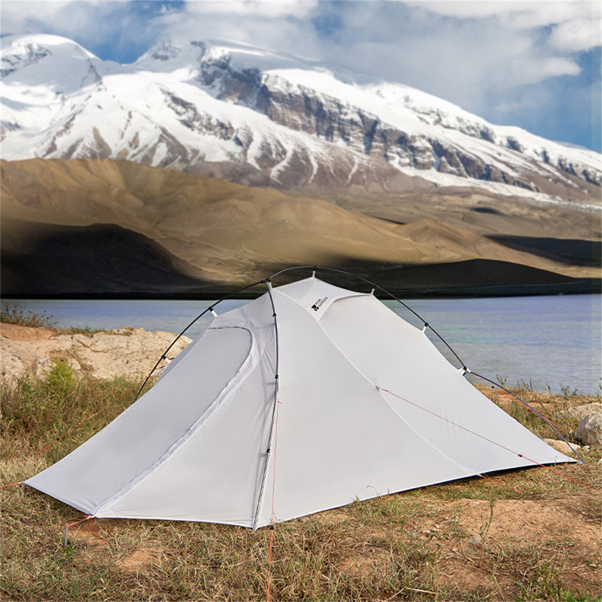 White tent set up in a natural landscape with mountains and water in the background