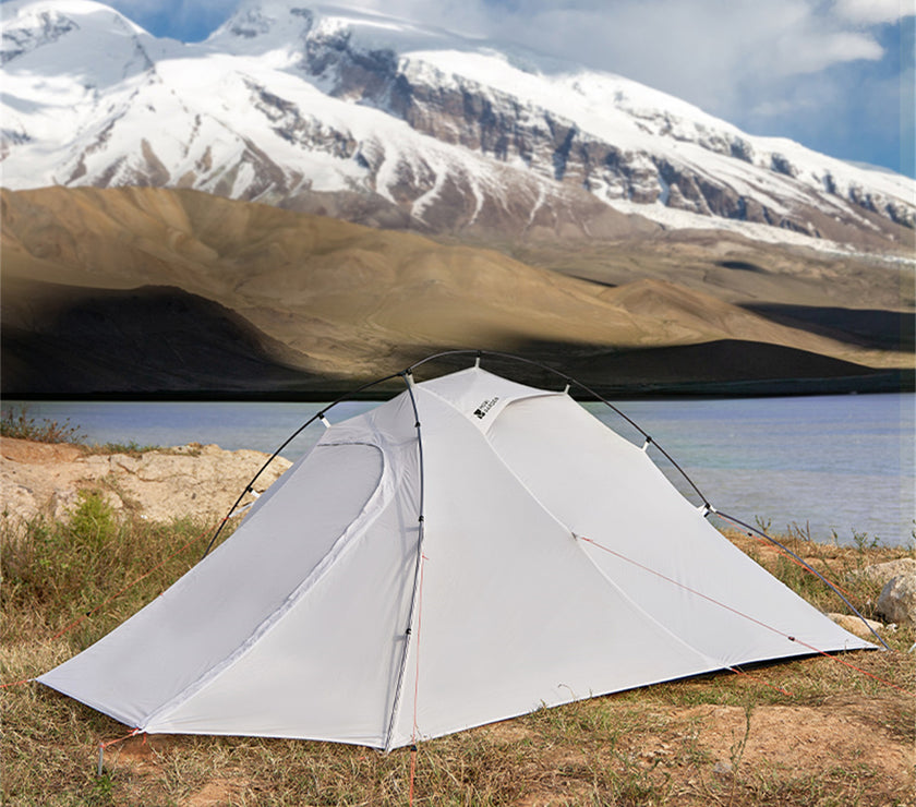 White tent set up in a natural landscape with mountains and water in the background