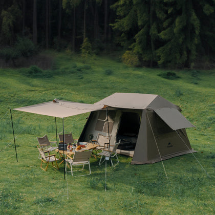 A brown Naturehike Village6.0 2 generation Quick Open Tent set up on a grassy field with an attached awning and outdoor furniture inside the tent's open entrance.