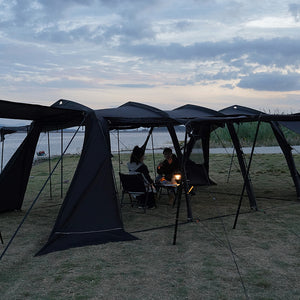 Two people sitting under a large black tent by a body of water with a cloudy sky.