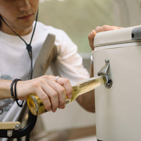 A guy using bottle opener on the side of Cooler to open beer
