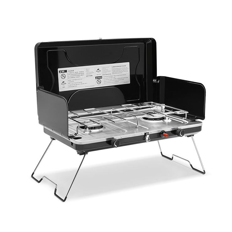 A foldable double burner camping stove made of stainless steel, displayed in its open state with a visible instruction label on the back, black control knobs, and a sturdy metal frame.