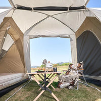 Camping scene with a tent, table, chairs, and outdoor furniture in a natural setting.