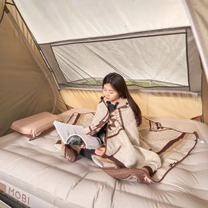 Person reading a book inside a tent with a blanket draped over them, featuring the Mobi brand.