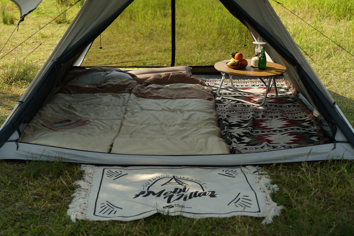Tent interior with bedding, rug, and small table on grass