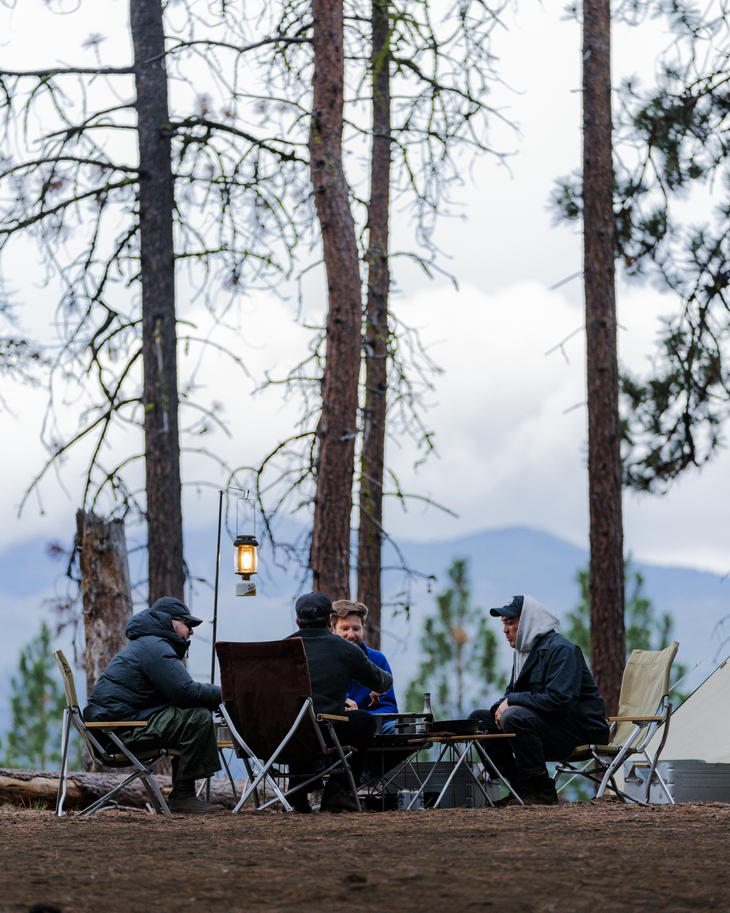 Snow Peak Low Beach Chairs around a low table at a dusk forest campsite, brown chair centre, lantern lit