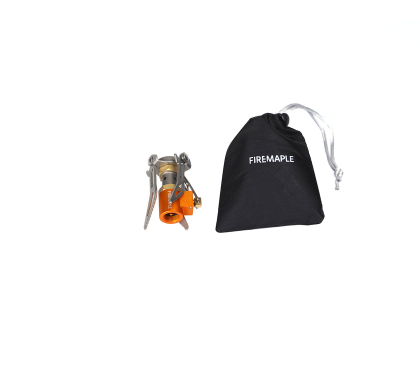 A portable foldable stove with a titanium body in silver color, alongside a black carrying bag with the brand 'Fire Maple' visible on it.