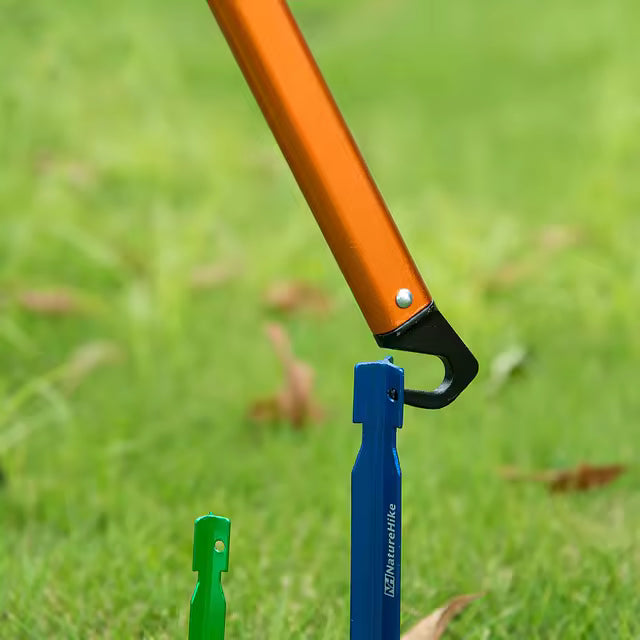 The hammer's hook pulling a blue Naturehike tent peg out of grass