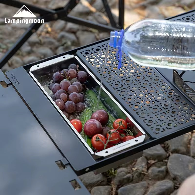 Campingmoon table with fruits and vegetables being rinsed under a stream of water.