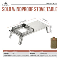 Dimensions labeled on the side of A silver stainless steel camping table with integrated windbreak and heat insulation, displayed alongside a carrying bag.