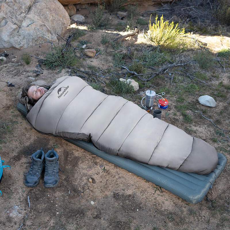 Person sleeping in a sleeping bag on a camping mat outdoors