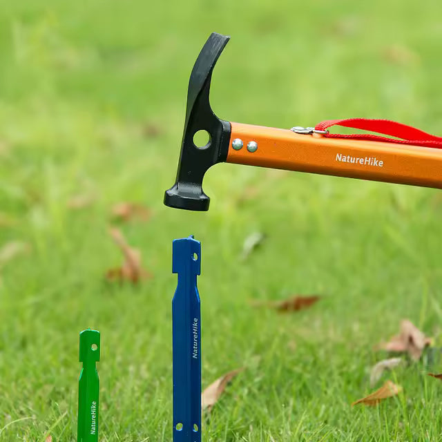 Naturehike orange camping hammer held above blue and green tent pegs in grass