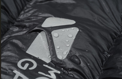 Close-up of a raincoat with water droplets on the hood, featuring a brand logo.