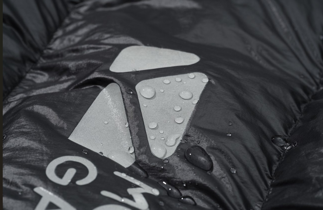 Close-up of a raincoat with water droplets on the hood, featuring a brand logo.