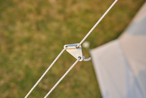 Close-up of a tent rope with a metal clip against a blurred grassy background