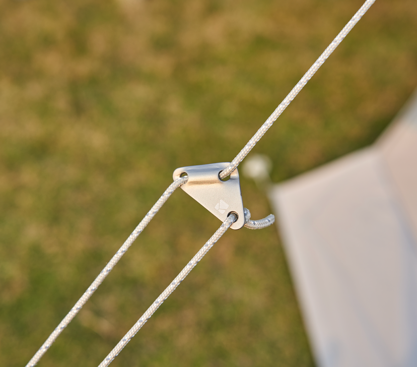 Close-up of a tent rope with a metal clip against a blurred grassy background