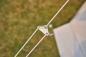 Close-up of a tent rope with a metal clip against a blurred grassy background