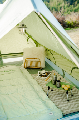 Camping setup inside a tent with a small table, pillows, and camping gear.