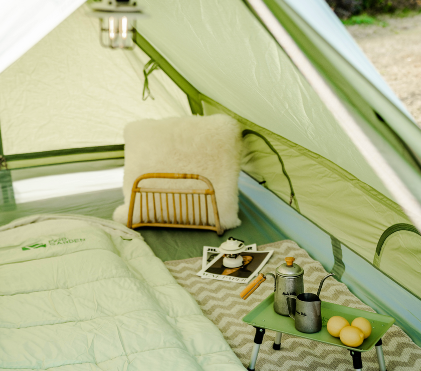 Camping setup inside a tent with a small table, pillows, and camping gear.