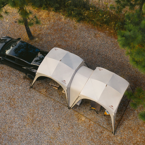 Two dome-shaped tents attached to a black car in a gravel area with trees.