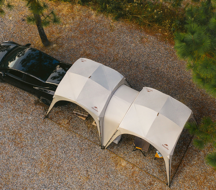 Two dome-shaped tents attached to a black car in a gravel area with trees.