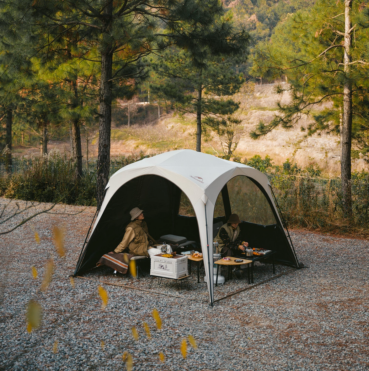 Two people sitting inside a portable camping shelter in a forest setting.