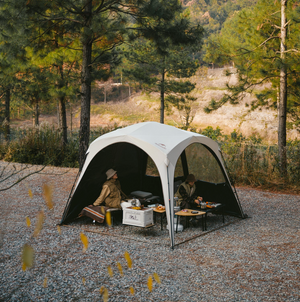 Two people sitting inside a portable camping shelter in a forest setting.