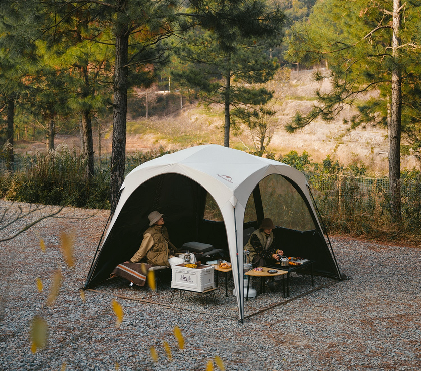 Two people sitting inside a portable camping shelter in a forest setting.