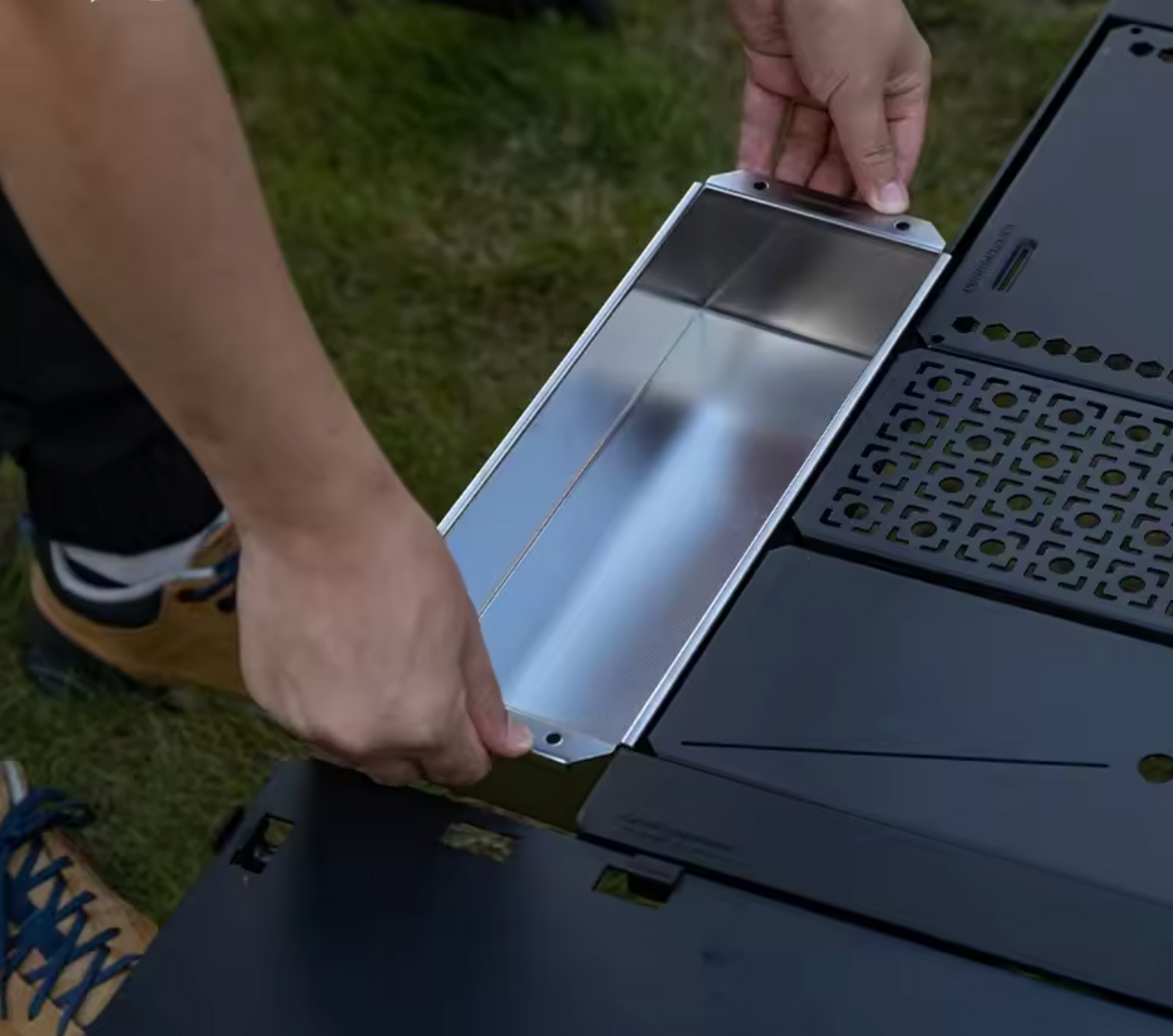 Person assembling a portable stove with a metallic pan on grass