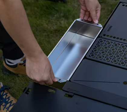 Person assembling a portable stove with a metallic pan on grass