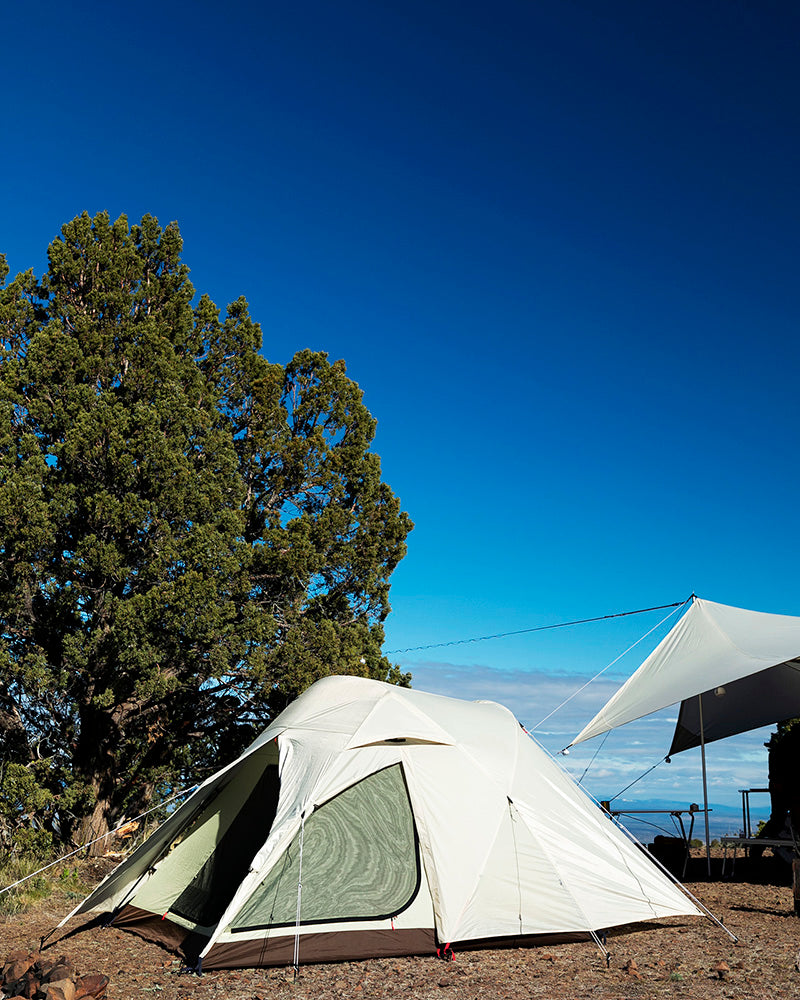 Snow Peak Alpha Breeze pitched on a ridge at dusk beside a tarp, juniper trees behind.