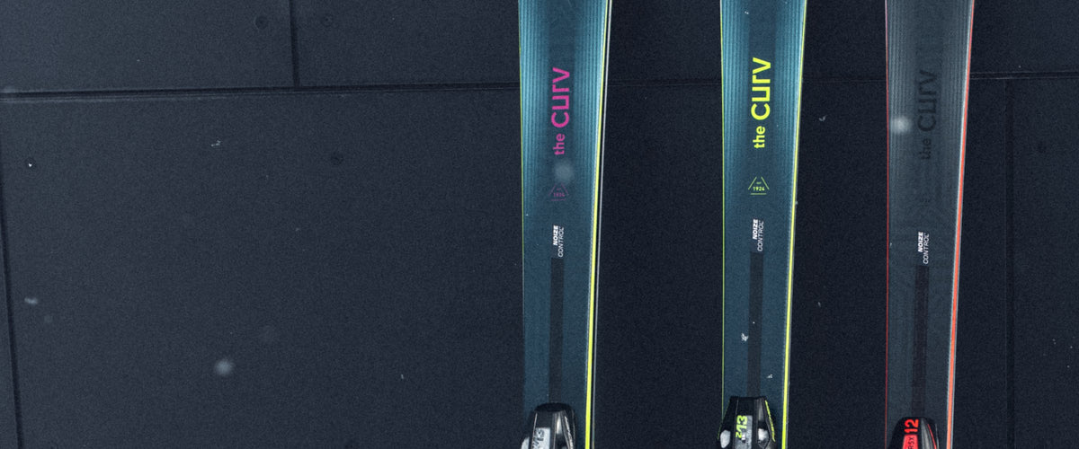 Three Fischer The Curv skis standing in snow against a dark wall