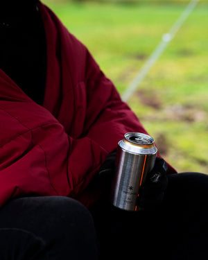 Snow Peak Shimo Can Cooler 350 held in a gloved hand outdoors, open can inside, camper wrapped in a red blanket