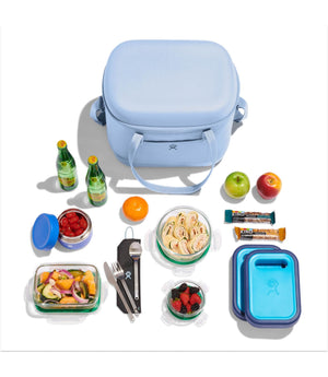 Blue lunch bag with food containers and snacks on a white background