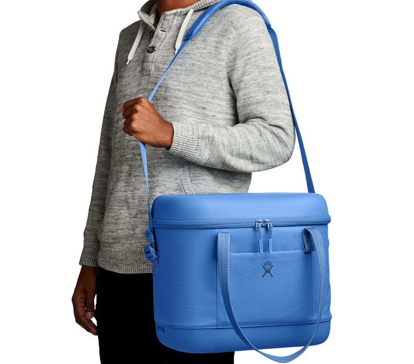 Person holding a blue cooler bag with a strap over their shoulder on a white background