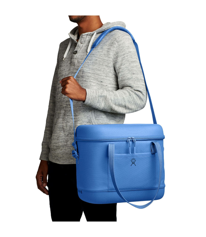Person holding a blue cooler bag with a strap over their shoulder on a white background