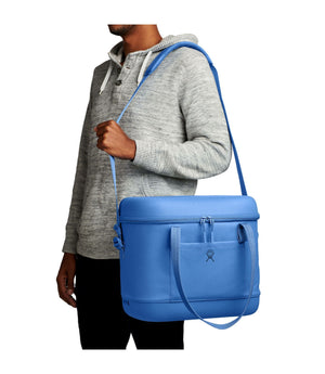 Person holding a blue cooler bag with a strap over their shoulder on a white background