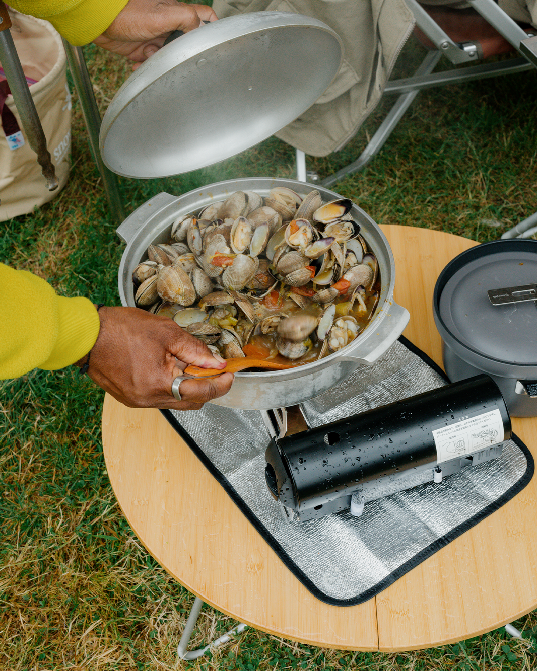 Snow Peak Home & Camp Burner GS-600 in black cooking a pan of steamed clams on a camp table outdoors
