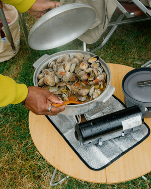Snow Peak Home & Camp Burner GS-600 in black cooking a pan of steamed clams on a camp table outdoors